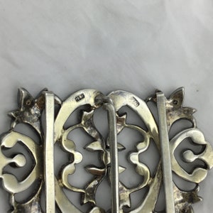 May include: A silver filigree belt buckle with a decorative design. The buckle has a hinged closure and is marked "925" on the back.