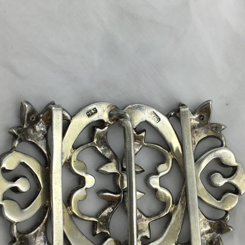 May include: A silver filigree belt buckle with a decorative design. The buckle has a hinged closure and is marked "925" on the back.