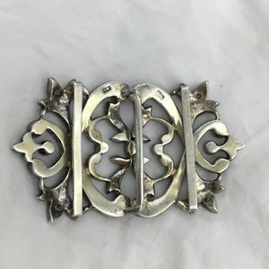 May include: A silver filigree belt buckle with intricate floral designs. The buckle is marked "925" on the back.