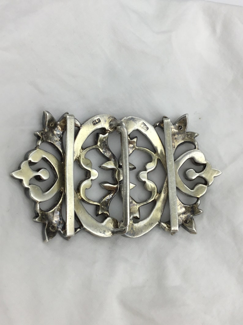 May include: A silver filigree belt buckle with intricate floral designs. The buckle is marked "925" on the back.