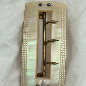 Puede incluir: Una hebilla de cintur&oacute;n de n&aacute;car blanco con una hebilla de lat&oacute;n y cuatro puntas. La hebilla tiene un patr&oacute;n de cuadros decorativos alrededor de los bordes.