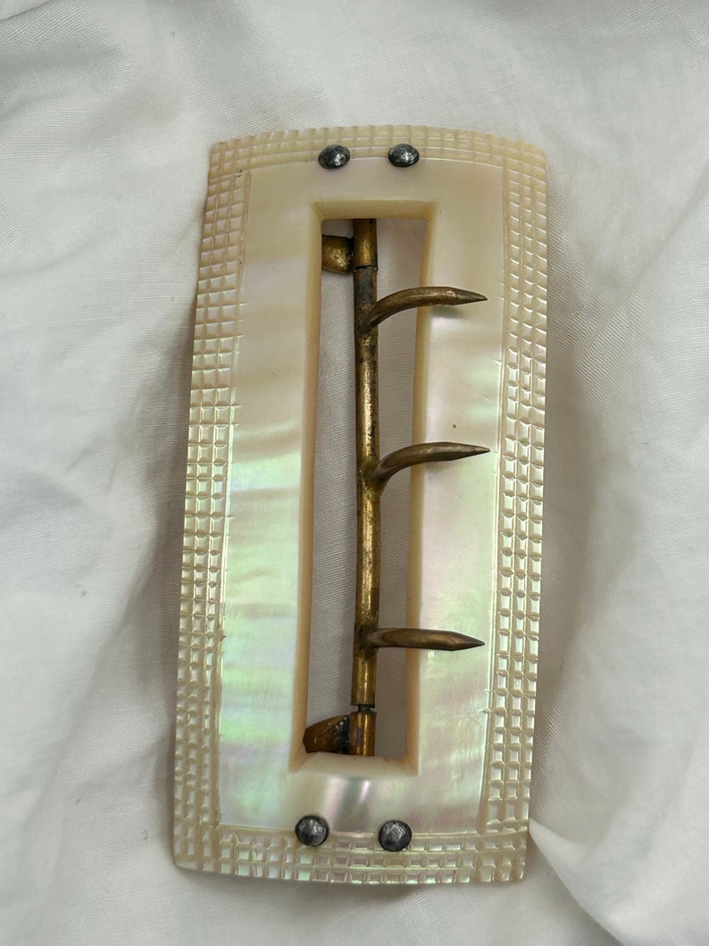 Puede incluir: Una hebilla de cintur&oacute;n de n&aacute;car blanco con una hebilla de lat&oacute;n y cuatro puntas. La hebilla tiene un patr&oacute;n de cuadros decorativos alrededor de los bordes.