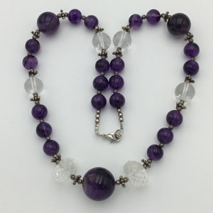 May include: A purple amethyst and clear crystal beaded necklace with a silver clasp. The necklace features alternating round and faceted beads.