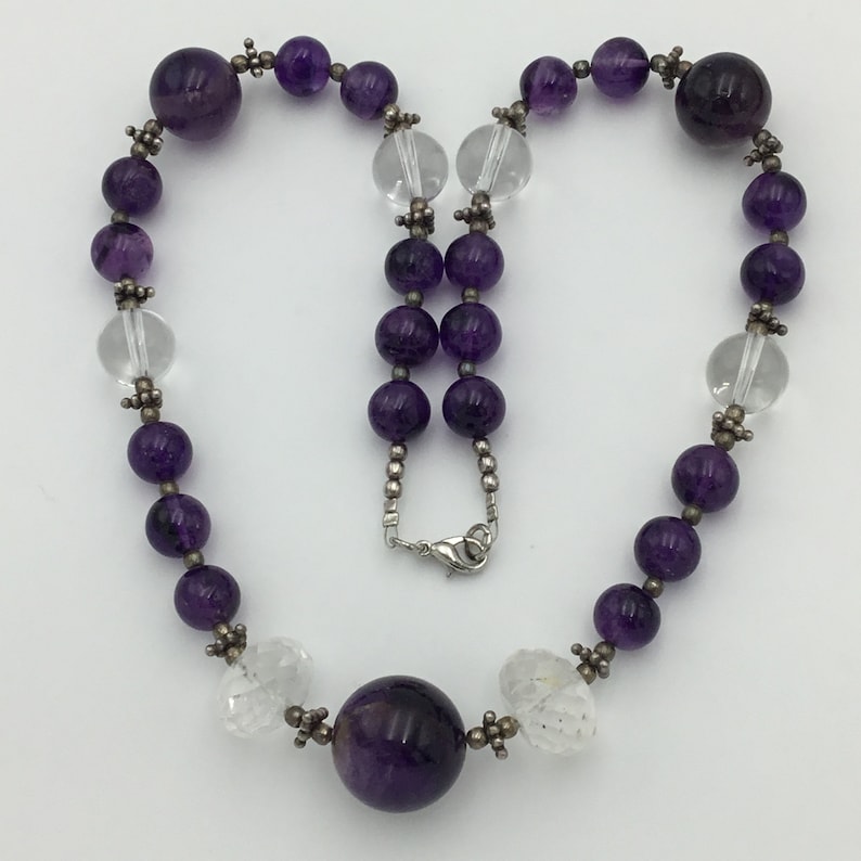 May include: A purple amethyst and clear crystal beaded necklace with a silver clasp. The necklace features alternating round and faceted beads.