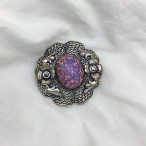 Puede incluir: Un broche de plata con una gran piedra de &oacute;palo iridiscente de forma ovalada engastada en un dise&ntilde;o de filigrana. El broche est&aacute; adornado con dos flores de plata m&aacute;s peque&ntilde;as.