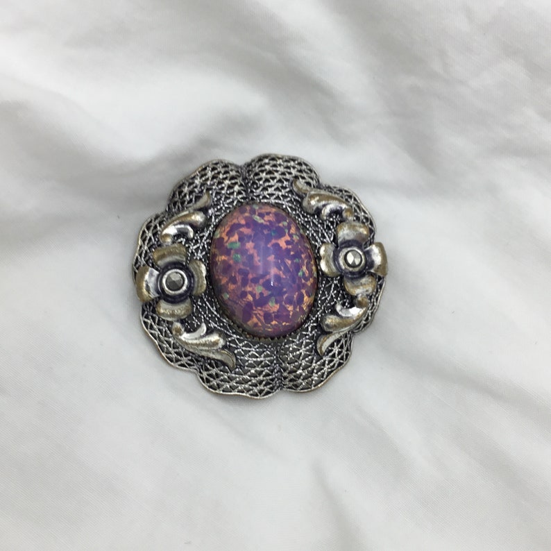 Puede incluir: Un broche de plata con una gran piedra de &oacute;palo iridiscente de forma ovalada engastada en un dise&ntilde;o de filigrana. El broche est&aacute; adornado con dos flores de plata m&aacute;s peque&ntilde;as.