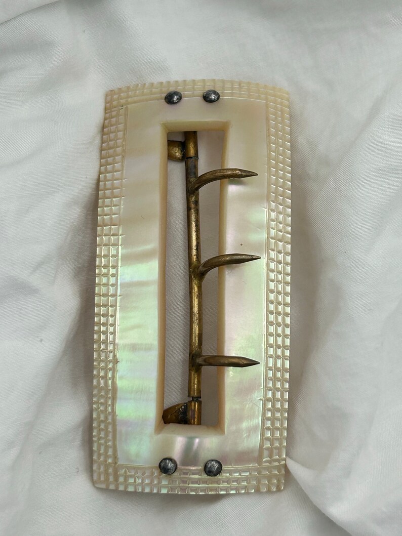 Puede incluir: Una hebilla de cintur&oacute;n vintage de n&aacute;car con un gancho de lat&oacute;n y cierre de leng&uuml;eta. La hebilla es rectangular y tiene una superficie texturizada.