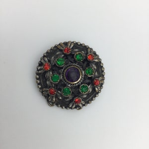 Arti e mestieri antichi, anni 1910-1920, ametista viola, rosso rubino, pasta di vetro verde e tono argento su spilla ornata in ottone. Misura 3 cm
