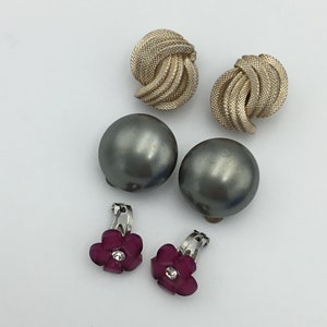 Może przedstawiać: Zestaw sześciu vintage kolczyków. Dwie pary są srebrne i mają wzór splecionego węzła. Jedna para jest szara i okrągła. Ostatnia para jest srebrna z wzorem różowego kwiatu i przezroczystym kryształem.