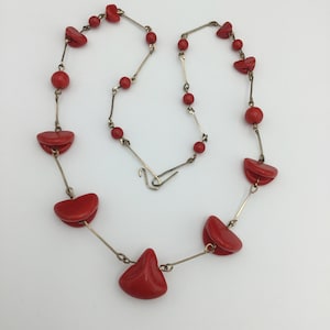 Könnte beinhalten: Eine Halskette aus roten Glasperlen mit einer silbernen Kette. Die Halskette besteht aus verschiedenen roten Glasperlen, darunter runde Perlen und größere, flache, herzförmige Perlen.