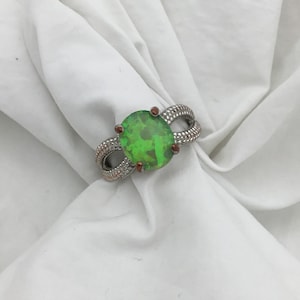 May include: A silver ring featuring a green oval-shaped gemstone set in the centre. The ring has a twisted band design.
