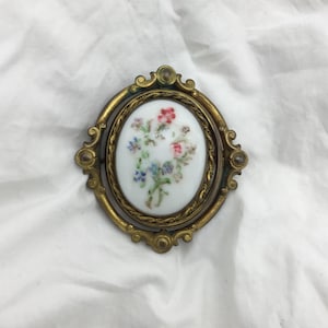 Spilla antica vittoriana girevole in ceramica bianca dipinta a mano, risalente al 1880 circa, con fiori in ottone dorato, grande spilla ovale, 6 cm x 5,5 cm nel punto più largo. I fiori indossano