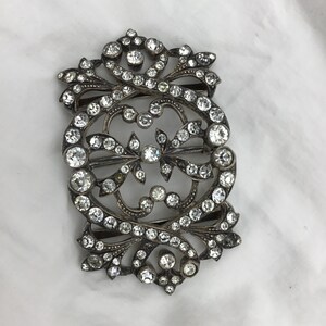 May include: A silver and crystal ornate buckle with a detailed floral design. The buckle is covered in small, clear crystals.