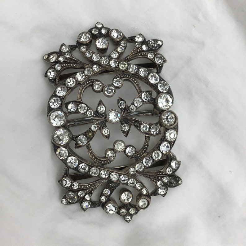 May include: A silver and crystal ornate buckle with a detailed floral design. The buckle is covered in small, clear crystals.