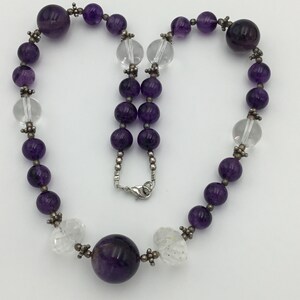 May include: A purple amethyst and clear crystal beaded necklace with a large amethyst pendant. The necklace is made with silver beads and a silver clasp.