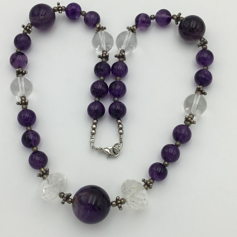 May include: A purple amethyst and clear crystal beaded necklace with a large amethyst pendant. The necklace is made with silver beads and a silver clasp.