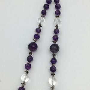 May include: A purple and clear crystal beaded necklace with a silver clasp. The necklace features alternating round amethyst and clear crystal beads.