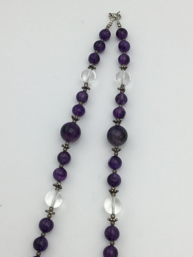 May include: A purple and clear crystal beaded necklace with a silver clasp. The necklace features alternating round amethyst and clear crystal beads.