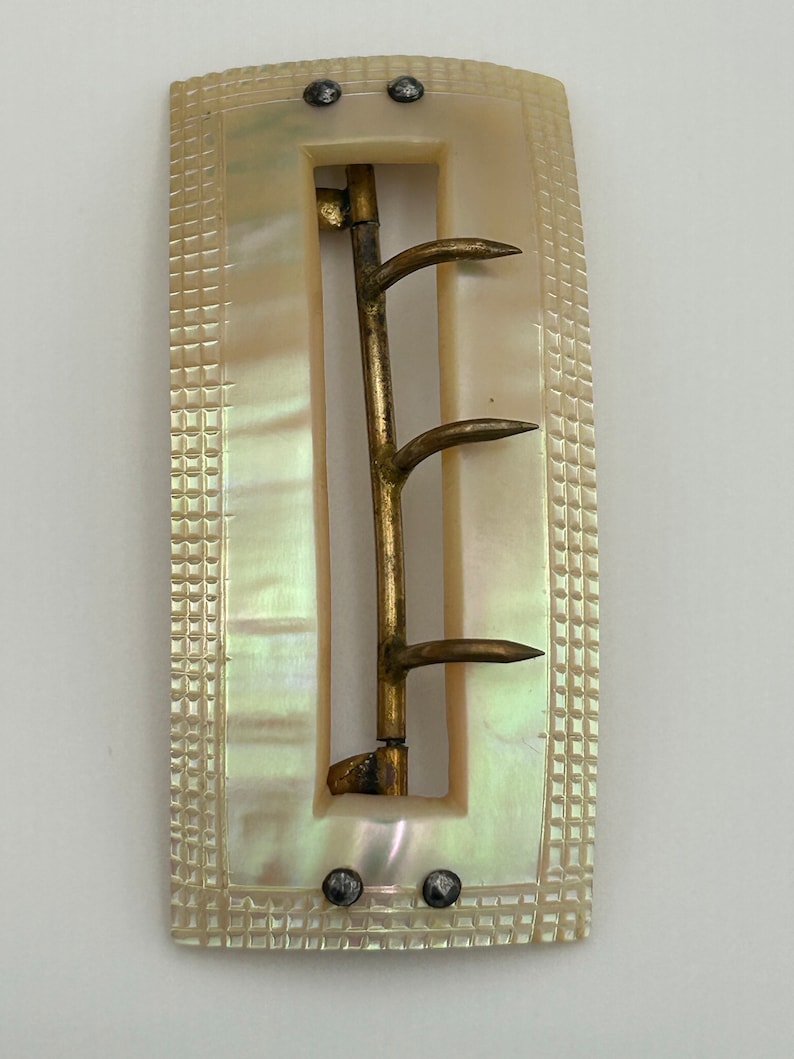 Puede incluir: Una hebilla de cintur&oacute;n vintage de n&aacute;car con un cierre de metal dorado. La hebilla tiene forma rectangular con una superficie texturizada y dos peque&ntilde;os remaches met&aacute;licos a cada lado.