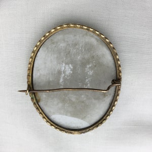 Pu&ograve; includere: Il retro di una spilla ovale in cammeo dorata con un cammeo in porcellana bianca. La spilla ha una spilla e una chiusura.
