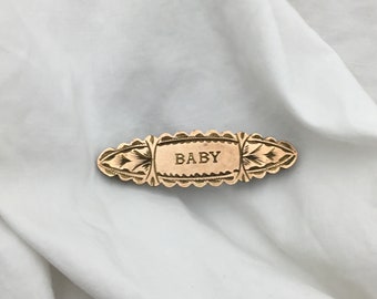 Antieke babynaam uit het begin van de 20e eeuw, gouden voorkant op een kleine broche van een koperen staaf. Afmeting 3,8 cm x 11 mm breedste. Smalle ovale vorm.