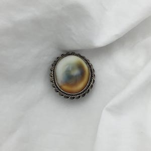 May include: A silver ring with a white and brown oval shell set in a twisted wire design.