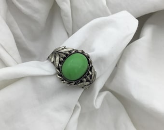May include: A silver ring with a green oval gemstone set in a leaf design.