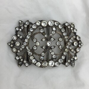 May include: A silver and crystal buckle with a floral design. The buckle is ornate and features a large number of small, clear crystals.