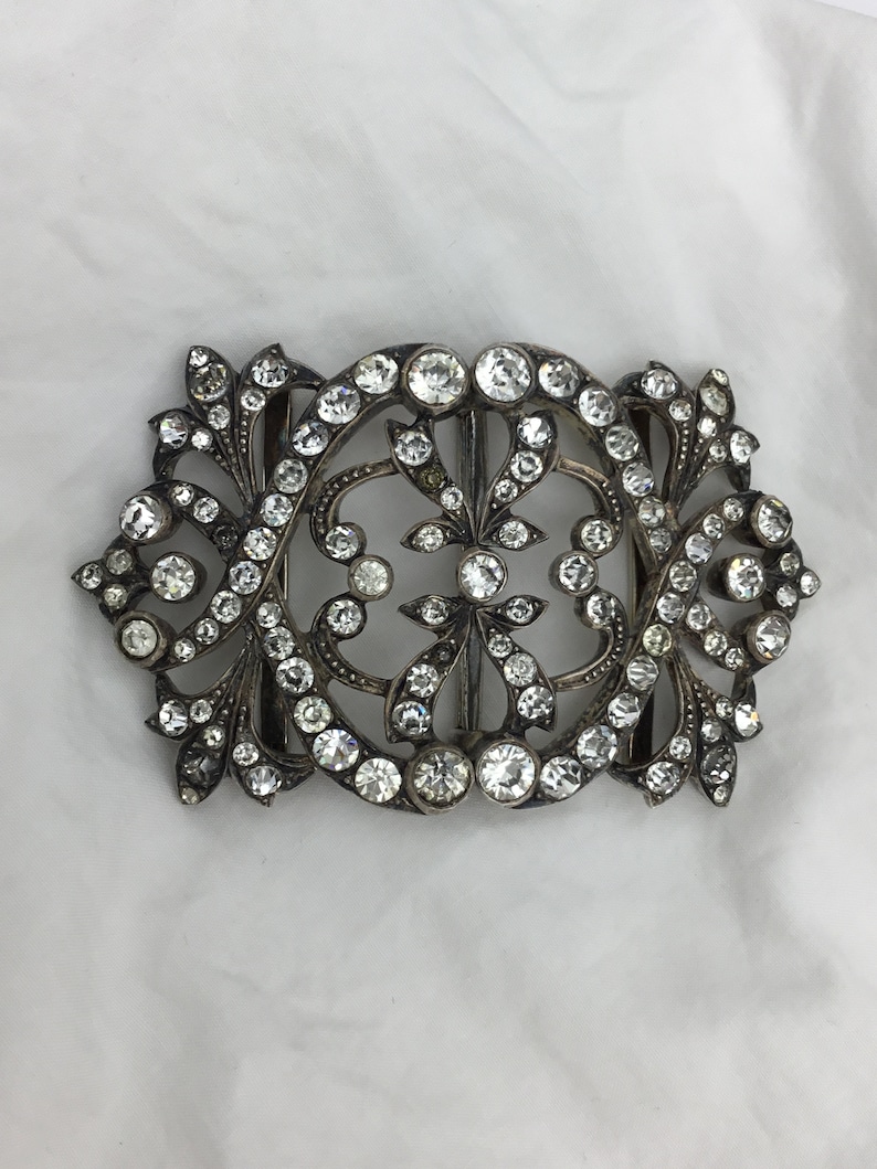 May include: A silver and crystal buckle with a floral design. The buckle is ornate and features a large number of small, clear crystals.