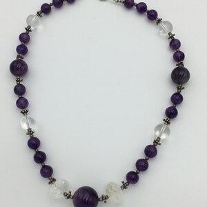 May include: A purple amethyst and clear crystal beaded necklace with a silver clasp. The necklace features a large amethyst bead in the centre.
