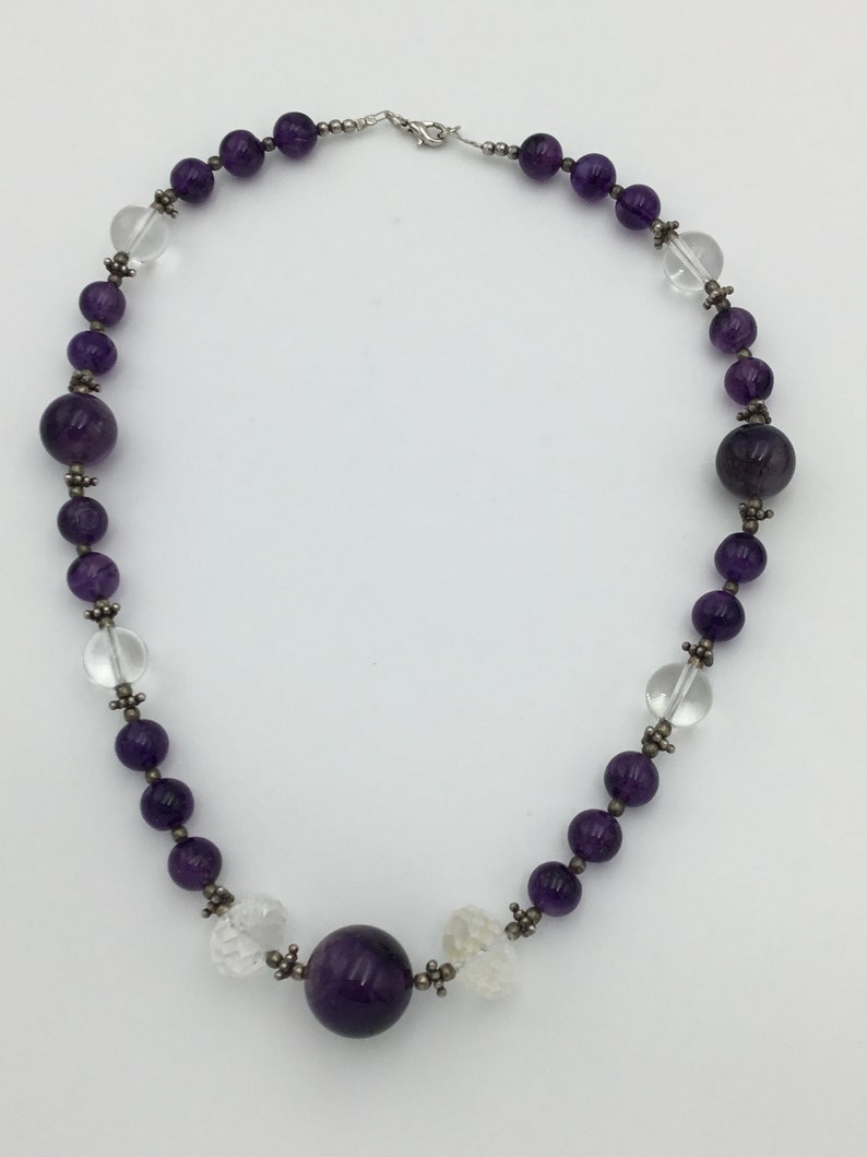 May include: A purple amethyst and clear crystal beaded necklace with a silver clasp. The necklace features a large amethyst bead in the centre.