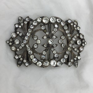 May include: A silver-toned ornate buckle with a floral design, set with clear rhinestones.
