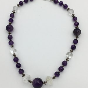 May include: A purple amethyst and clear crystal beaded necklace with a large amethyst bead in the centre.