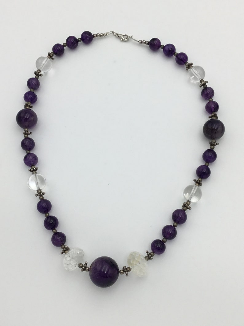 May include: A purple amethyst and clear crystal beaded necklace with a large amethyst bead in the centre.