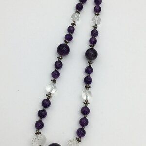 May include: A purple and clear crystal beaded necklace with a large purple crystal pendant. The necklace is made of faceted beads and has a silver clasp.
