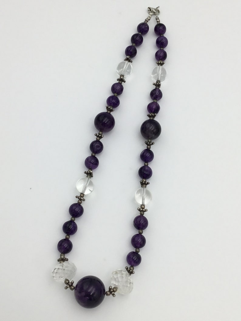 May include: A purple and clear crystal beaded necklace with a large purple crystal pendant. The necklace is made of faceted beads and has a silver clasp.