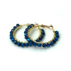 May include: A pair of gold hoop earrings with blue iridescent beads. The earrings are made of wire and have a simple design.