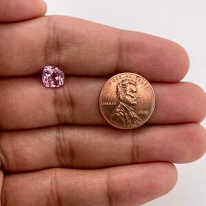 May include: A pink square-shaped gemstone, approximately the size of a US penny.