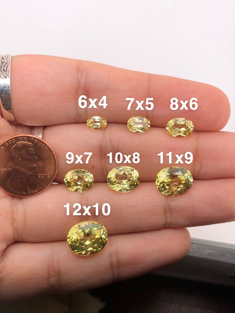 May include: A set of yellow oval gemstones of different sizes, labelled with their dimensions in millimetres. The gemstones are arranged in a row on a hand, with the smallest gemstone at the top and the largest gemstone at the bottom. The gemstones are all cut in a similar style, with a smooth, polished surface.
