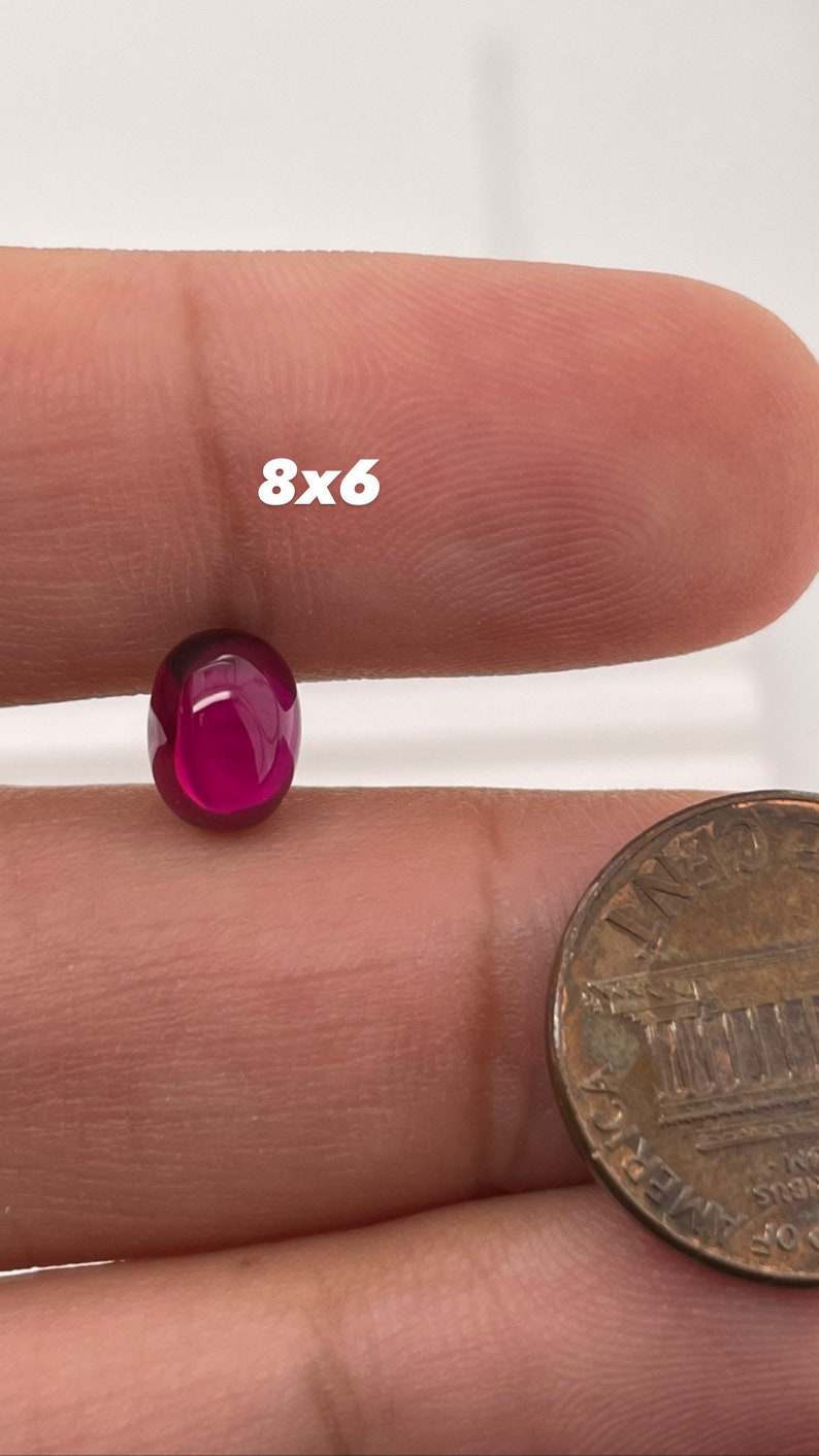 K&ouml;nnte beinhalten: Nahaufnahme eines tiefrosa ovalen Cabochons, etwa 8 mm x 6 mm, in einer Hand gehalten, neben einem US-Cent zur Gr&ouml;&szlig;enveranschaulichung.