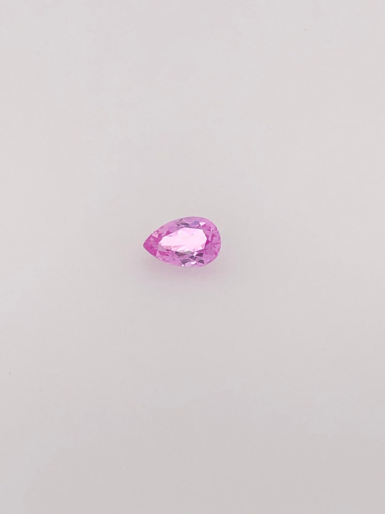 May include: A pear-shaped pink gemstone with facets.