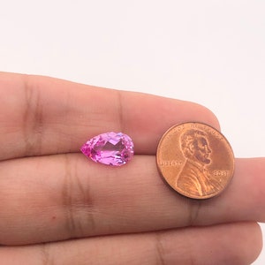 May include: A pink pear-shaped gemstone next to a US penny for size comparison.