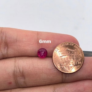 May include: A 6mm round red ruby gemstone with a star-shaped pattern inside. The ruby is next to a US penny for size comparison.