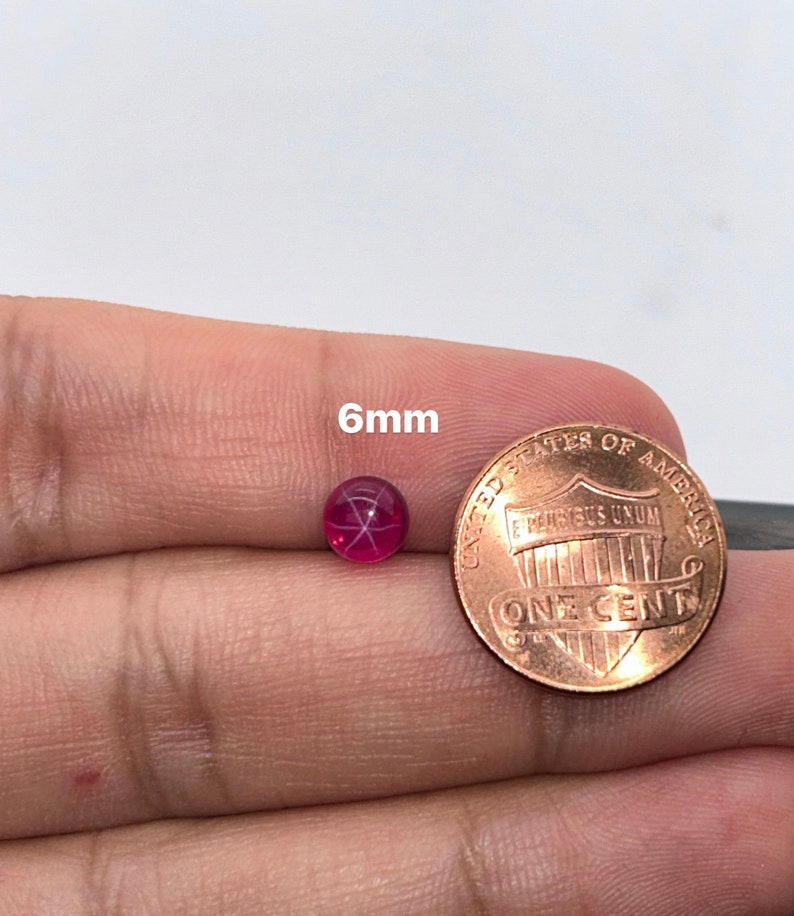 May include: A 6mm round red ruby gemstone with a star-shaped pattern inside. The ruby is next to a US penny for size comparison.