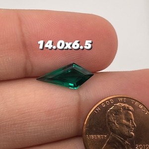 May include: A vibrant emerald-green gemstone with a kite-like shape, measuring 14.0 x 6.5. The gem is held near a penny for size comparison. The text "14.0x6.5" is overlaid on the image.
