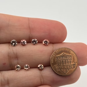 Op de afbeelding: Zeven kleine, ronde, gefacetteerde edelstenen in roze en bruine tinten. De edelstenen zijn in een rij op een hand gelegd, met een Nederlandse cent als maatstaf.