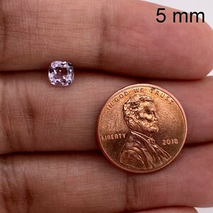May include: A 5 mm pink gemstone, a square cut, is shown next to a US penny for size comparison.  "In God We Trust" and "Liberty" are visible on the penny.