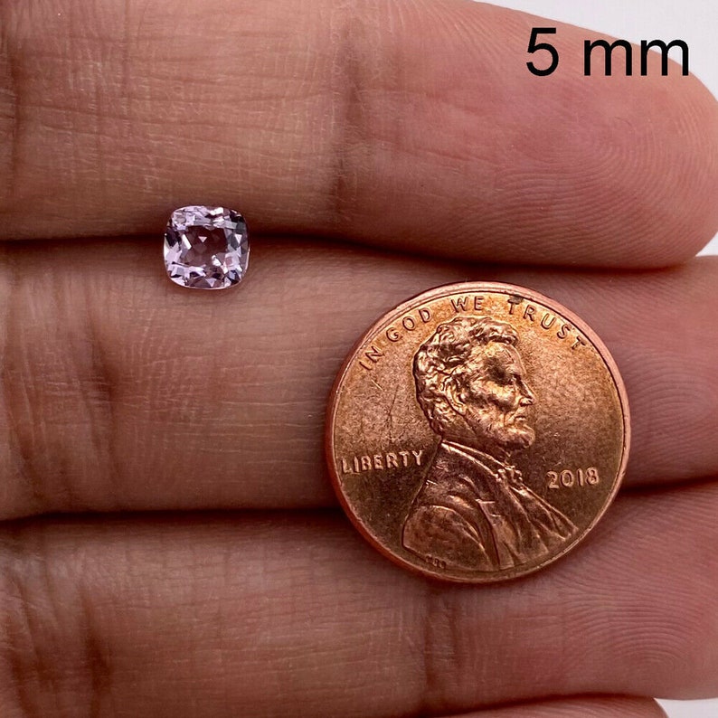May include: A 5 mm pink gemstone, a square cut, is shown next to a US penny for size comparison.  "In God We Trust" and "Liberty" are visible on the penny.
