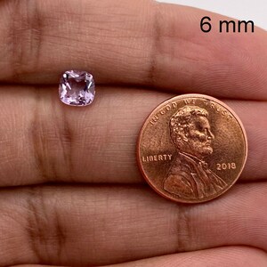 May include: A light pink cushion-cut gemstone measuring 6 mm in diameter, shown next to a US penny for size comparison.