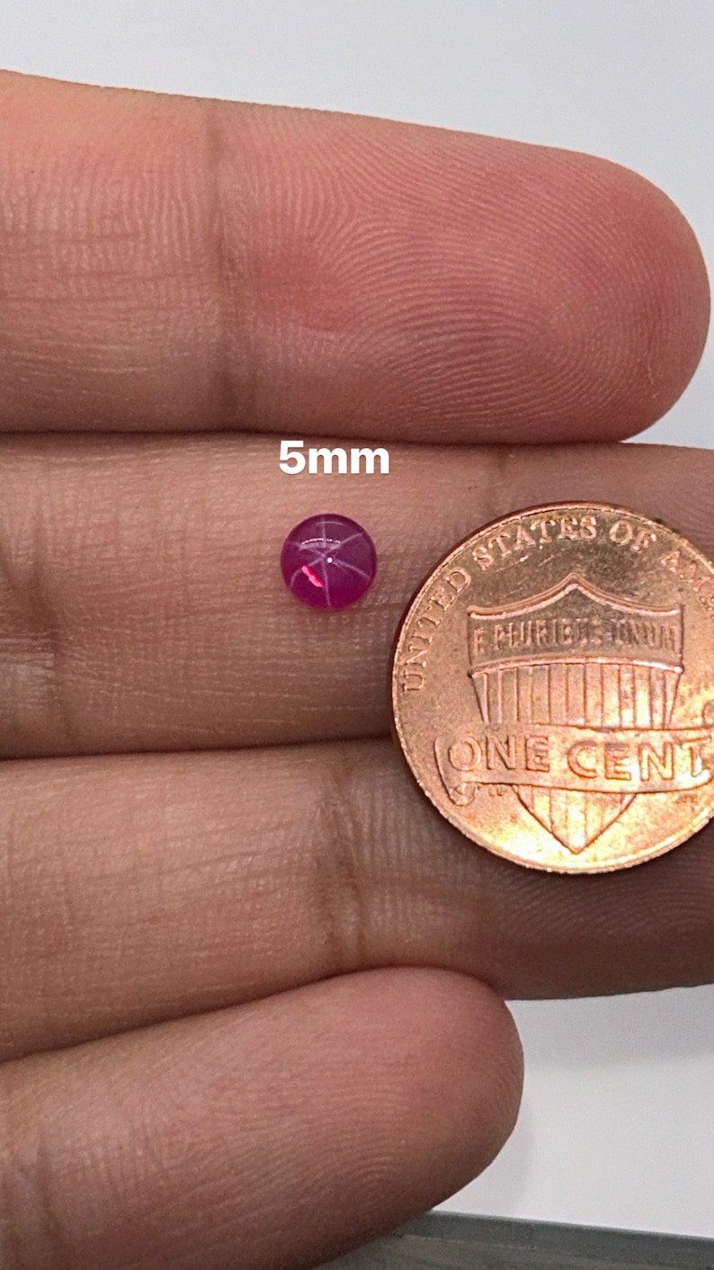 May include: A 5mm pink star ruby gemstone, next to a US penny for size comparison.